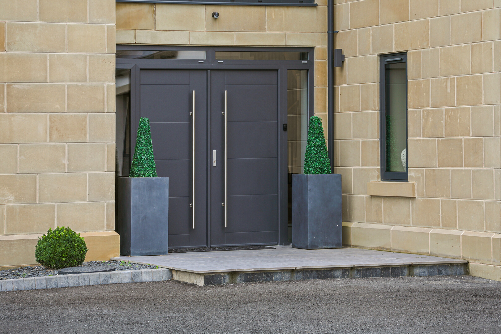 This is a close-up shot of the front doors with two plant pots and plants to either side of the two large grey doors.