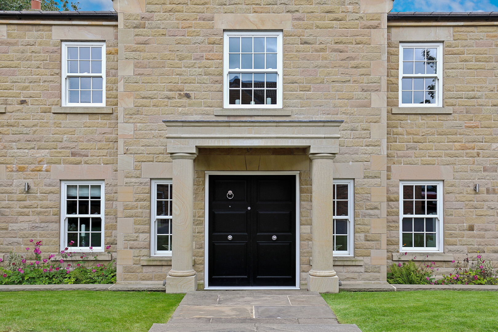 This shot is a direct image of the front of the Georgian-style house. This image shows the front door, stone pillar posts and windows. This also includes the facade of the building.