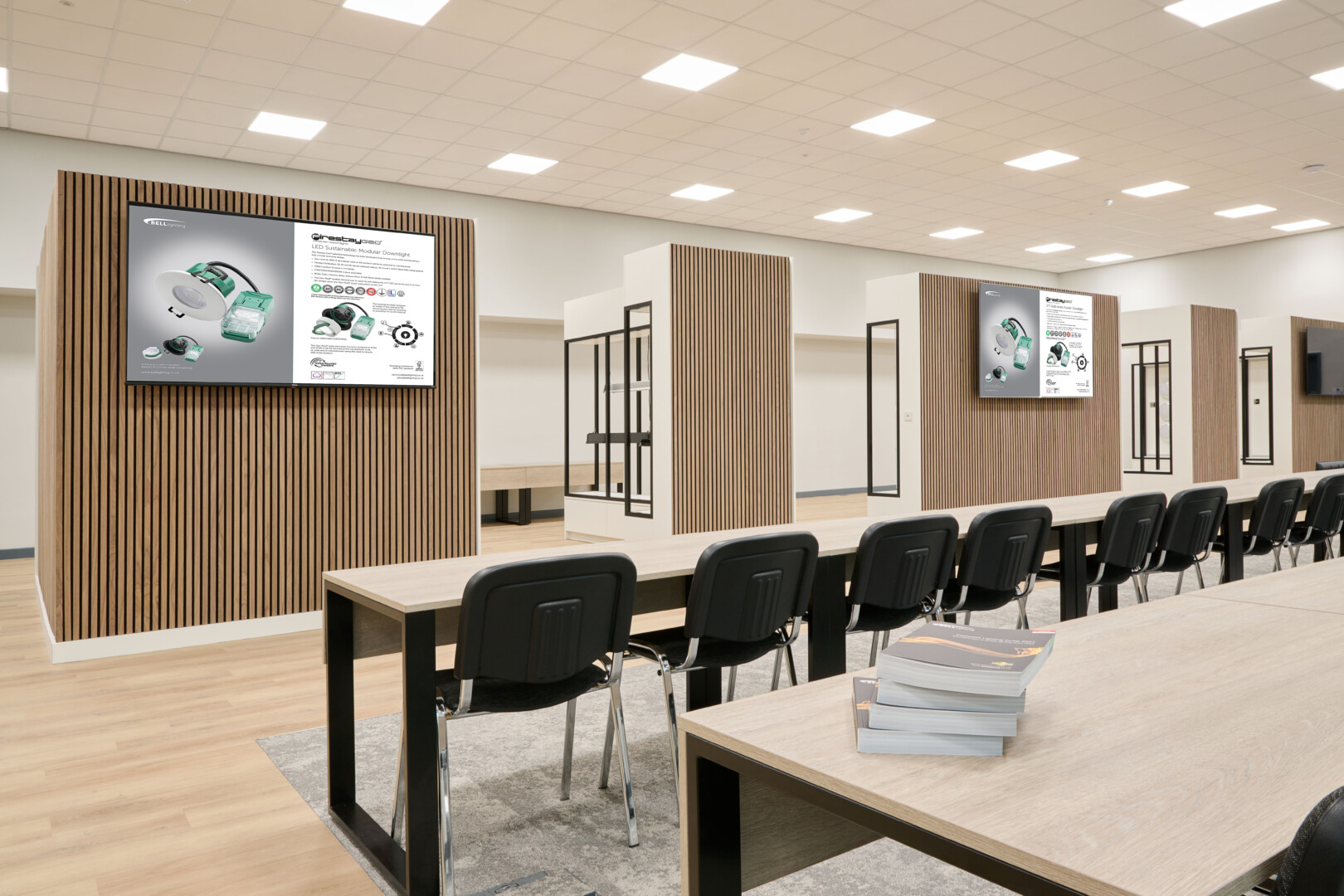 An image of the whole showroom space which has long tables, chairs, three televisions attached to the units and five units displaying products.