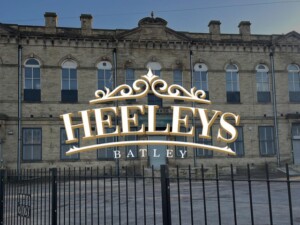 An image of the new Heeley's logo that is over a darker image of the building. The white writing gives a nice contrast to the background image.