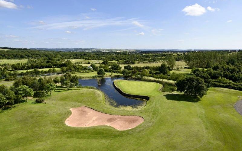 An aerial shot of one of the holes on the course at Willow Valley Golf Club. In the picture you can see the blue sky, a lake and a bunker, as well as the fairway.