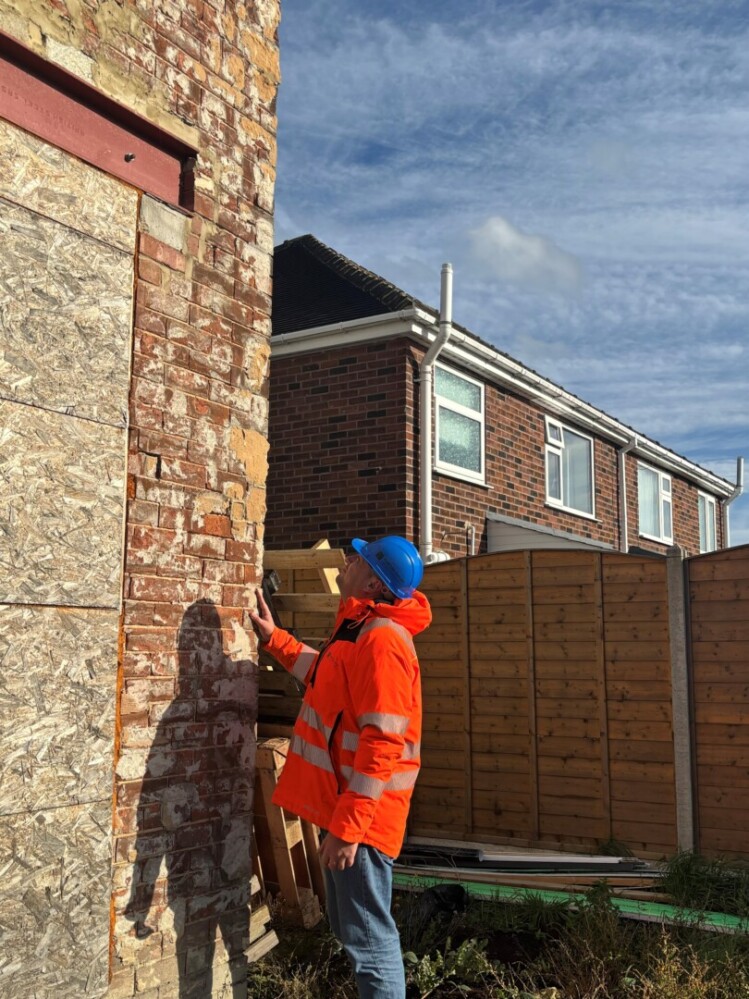 An image of Associate Director at MWA, Ryan Lewis, on site of a project wearing an orange high visibility jacket and a blue hard hat. He is looking towards the wall of the building.